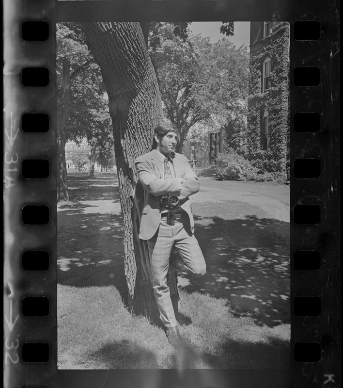 Man with camera leaning against a tree on Tufts University campus