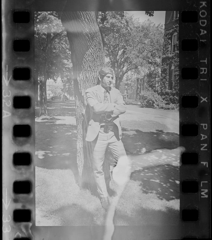 Man with camera leaning against a tree on Tufts University campus