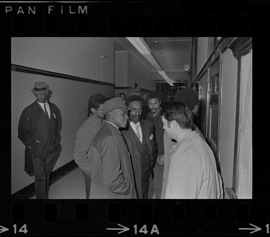 Group of men standing and talking in Boston State College hallway during Black student protest