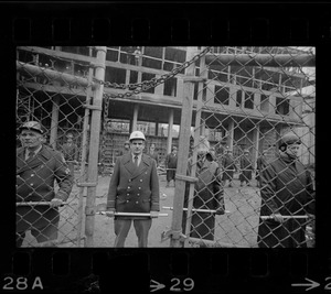 Policeman seen through gate at Tufts University dormitory construction site, center of student opposition
