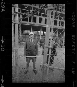 Policeman seen through gate at Tufts University dormitory construction site, center of student opposition