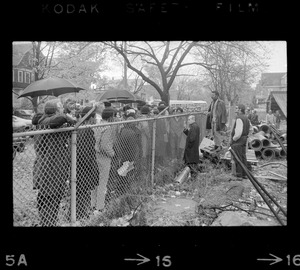 Protesters standing by a fence bordering the Tufts University dormitory construction site that is at the center of student opposition and speaking to a man on the other side, possibly Rev. Robert Drinan