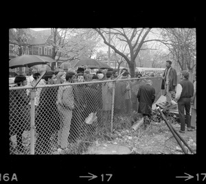 Protesters standing by a fence bordering the Tufts University dormitory construction site that is at the center of student opposition and speaking to a man on the other side, possibly Rev. Robert Drinan