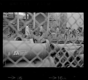 A group of people, seen through a fence, walking through the Tufts University dormitory construction site that is at the center of student opposition