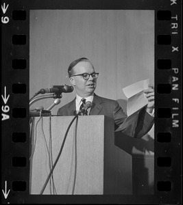 A man speaking from a podium while looking at his notes being held in his hand