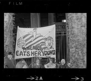 Student protesters sitting under an 'America Eats Her Young' banner