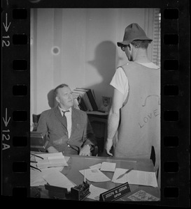 Captain Joseph W. Jordan of the Boston vice and narcotics bureau, speaking to a man while seated at his desk