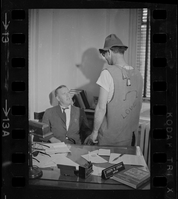 Captain Joseph W. Jordan of the Boston vice and narcotics bureau, speaking to a man while seated at his desk