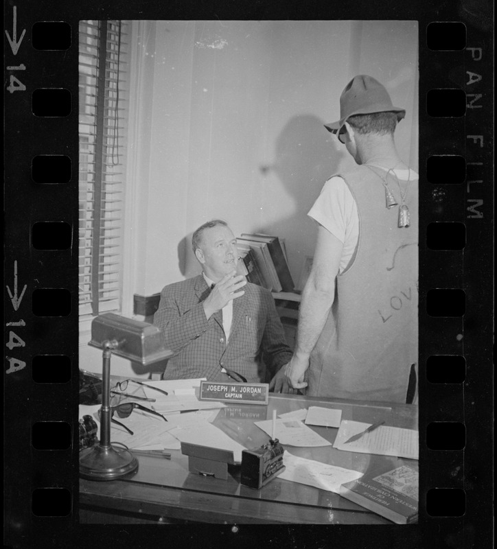 Captain Joseph W. Jordan of the Boston vice and narcotics bureau, speaking to a man while seated at his desk