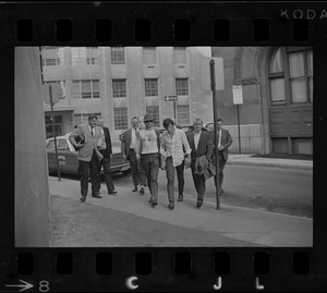 A group of men leading a man (center) across a street