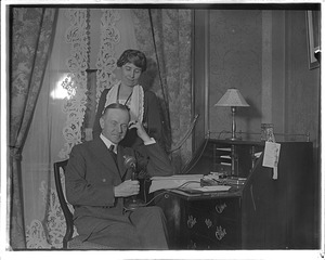 His wife stands by while Pres. Coolidge takes a call