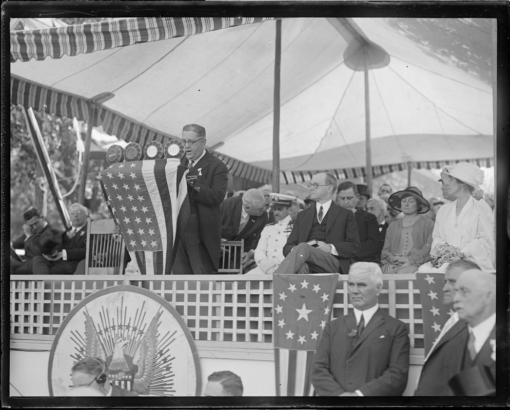 Pres. and Mrs. Coolidge seated look on while Mayor Quinn of Cambridge speaks at the podium, Cambridge