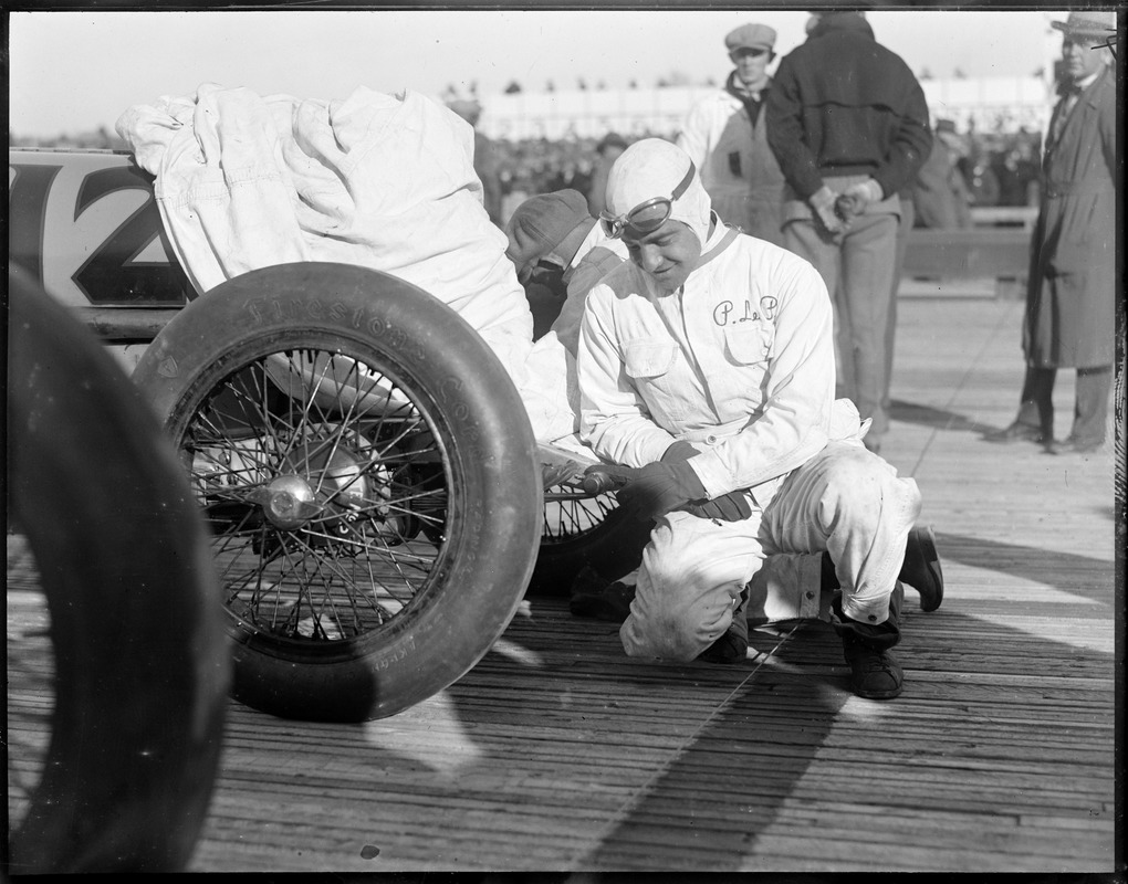 Famous auto racer R. De Palma pins his baby's shoe on his auto for luck before race in Rockingham, N.H.