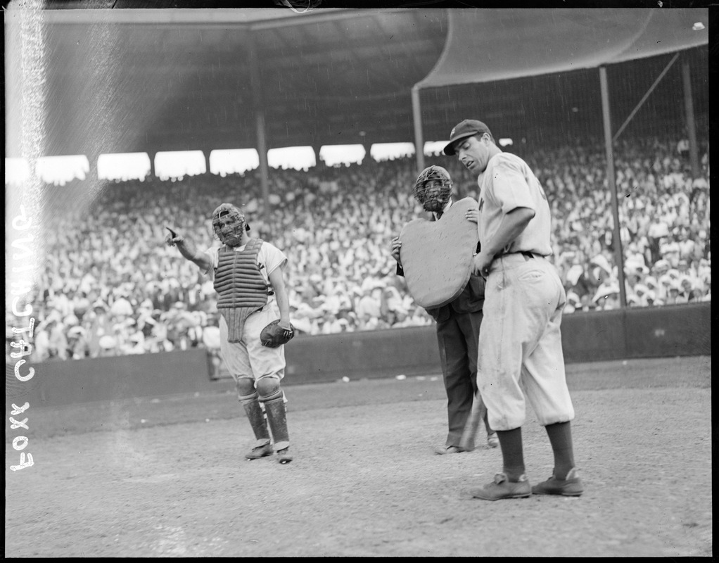 Catcher Jimmy Foxx of the Red Sox points to the outfield as DiMaggio of the Yankees and the umpire looks on