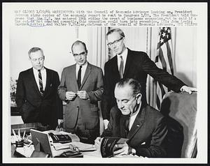 With the Council of Economic Advisers looking on, President Johnson signs copies of the economic report he sent Congress 1/20. The President told Congress that the U.S. has entered 1964 riding crest of business expansion. But he said if a tax cut is not enacted promptly, this expansion could turn into recession . LTR: John Lewis; Gardner Ackley; and Walter W. Heller, chairman of the Council of Economic Advisers.