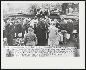Forced to Leave-- A large group carrying personal belonging stands beside an Army duck here today waiting to be loaded aboard and evacuated from this flood-ridden city. A group of nuns waits with the group which was taken to higher ground to Sioux City, Ia. across the river from South Sioux City.