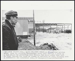 Dike Break--A floodworker watches water from the flooding Mississippi river pour through a break in a dike which was protecting Rock Island. The water pours from left to right through the break at corner of building at left, flooding both a residential and industrial area.