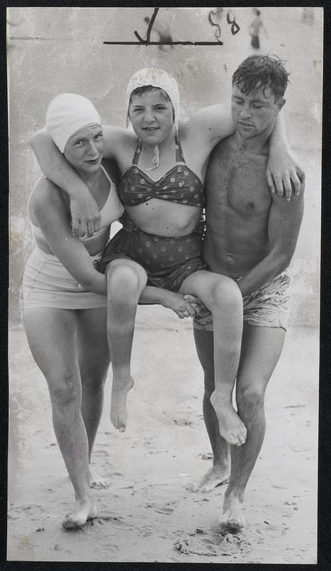 Vacationing Polio Victim at the country's first camp for children crippled from infantile paralysis is carried from the water at Plum island. Diana Simons, 14, of Haverhill is helped by Physiotherapist Janice Hodgkins, West Roxbury, and Counselor Sheldon Allen, Lynn.