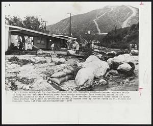 Boulders and Mud Threaten Homes--Volunteer workers battle to keep mud and boulders washing down from nearby mountains from damaging houses on the northern outskirts of this foothill city today. Some residents evacuated their homes as heavy rains started the slides on watersheds recently burned over by forest fires on Mt. Wilson and Monrovia Peak.