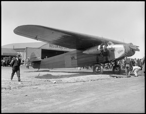 Byrd's South Pole plane before they put pontoons on it. East Boston Airport. B.A.C. hangar in back, a Fokker trimotor plane, and people.