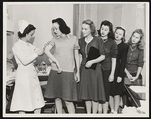 University of Chicago Students Nurse Martha Cooley injects Jean Roff, freshman student, with the new type influenza vaccine, discovered by Rockefeller Foundation research workers, as other students wait their turns. The widespread outbreak of influenza has given the authorities here an opportunity to observe the results of the new vaccine. About 500 students of the school are being inoculated in the test.