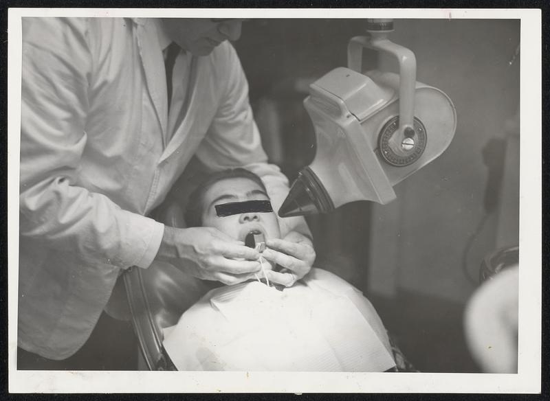 X-Raying a handicapped child is a difficult procedure, particularly one with cerebral palsy. Here, Dr. William Segal of Somerville adjusts film tab in tranquilized patient's mouth.