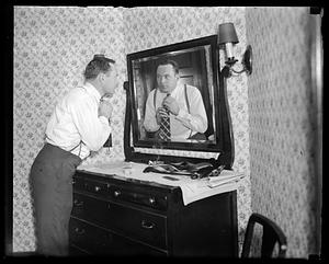 A man adjusting his tie, looking in a mirror