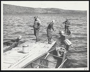 A man goes out onto the water on a boat while two men stand on the dock