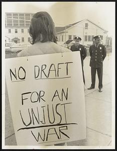 Outside Boston Army Base Anti-draft demonstration From the rear it appears to be a girl. No not so, its a long-haired (man) demonstrator. Dept of Defense Police stand-by.