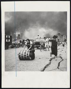 Japs Flee Fukui Earthquake Japanese women, one rolling a container and the other carrying a bag, seek haven with household goods as smoke rises from fires caused by the June 28 earthquake Fukui, Japan. Woman at right leaps crack in paved street.