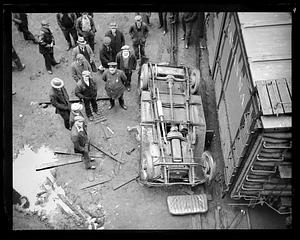 People standing around an overturned car by a railroad car