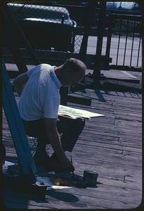 Artist reaching for paint on pier