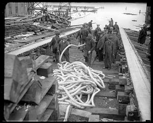 A group of men with a thick rope, possibly at a shipyard