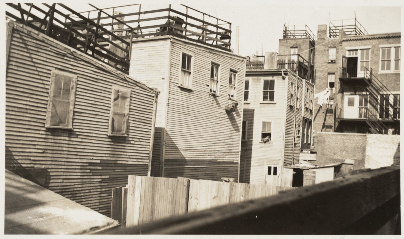 The exterior of tenement buildings on Salem Street in Boston's North End. The wooden houses are packed close together and are in need of upkeep.