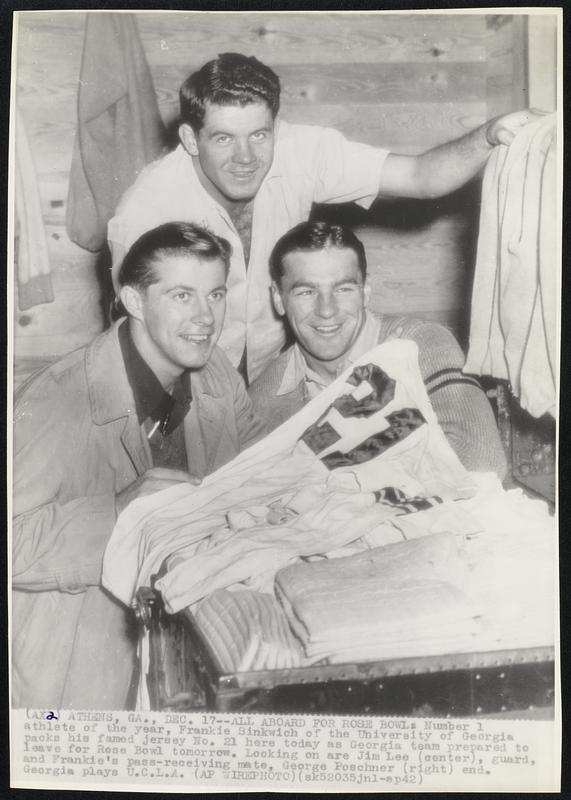 All Aboard for Rose Bowl: Number 1 athlete of the year, Frankie Sinkwich of the University of Georgia packs his famed jersey No. 21 here today as Georgia team prepared to leave for Rose Bowl tomorrow. Looking on are Jim Lee (center), guard, and Frankie's pass-receiving mate, George Poschner (right) end. Georgia plays U.C.L.A.