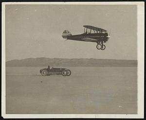 Plane Races Car On The Mojave Desert. The “dry lake” at Murco, Calif., in the heart of the Mojave Desert, is a good place to step on the gas without fear of traffic. Photo shows Louis Moore in his straight-eight Miller racing car, trying to beat out Dick Dodge, millionaire sportsman, in his tapered wing Waco airplane. At the moment this picture was made, both car and plane were clocked at 145 miles an hour.