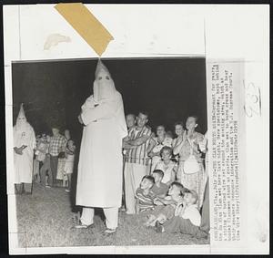 The Klan Meets Again-Dormant for years, the Ku Klux Klan met here last night. Here spectators, kept behind a string of barbed wire set around the meeting area, watch as hooded Klansmen stand as guards. Klan met to burn cross and hear their speakers denounce integration and the U.S. Supreme Court.