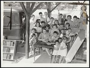 Outdoor Library at Stearns playground, Newton. Mrs. Lucy Audolina, Newton library, is shown lending books from the moving library recently established by her department. The system of playground distribution raised library circulation figures by more than 1000 during July.