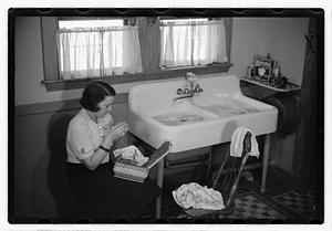 A woman sewing next to a sink full of laundry