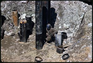 Worker crouching among upright cylinders at construction site, Boston