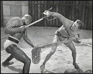 Spartacus Gladiator Kirk Douglas, with a Thracian sword, fights to the death with giant Negro Woody Strode, who uses a five-foot-long trident and net. A scene from "Spartacus," $12,000,000 Bryna Production co-starring Douglas, Laurence Olivier, Miss Simmons, Tony Curtis, Charles Laughton, Peter Ustinov and John Gavin. Filmed in Super Technirama-70 for release by Universal-International.
