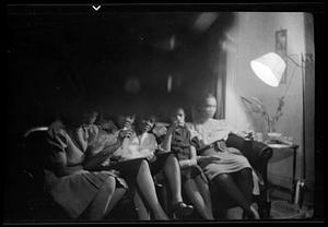 Five women sit on a couch by a lamp