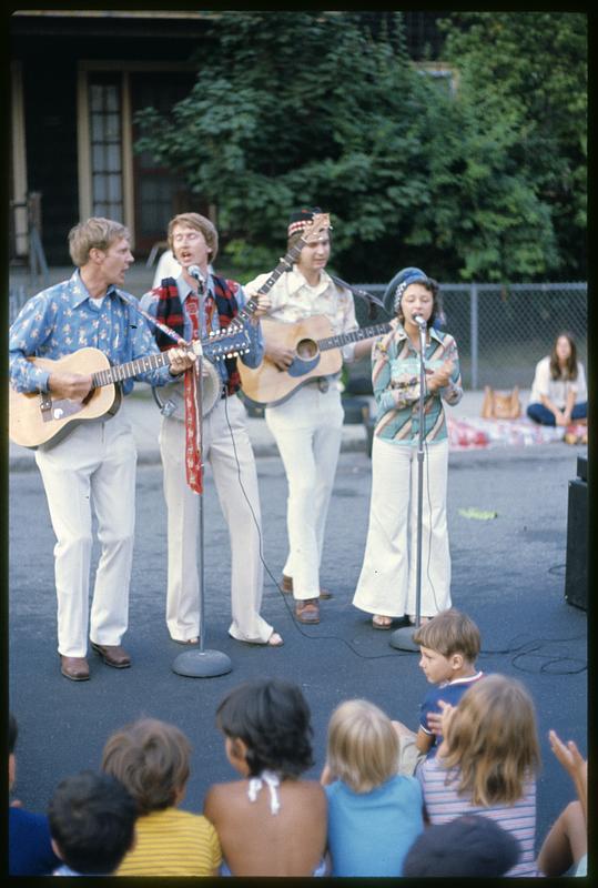 Band with guitars, banjo, and singer performing on street, likely Boston