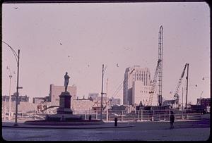 Cranes in front of buildings, Samuel Adams statue in foreground