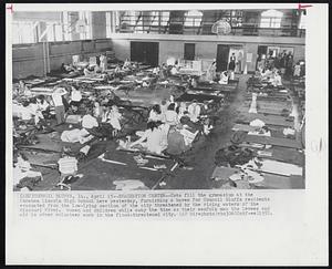 Evacuation Center--Cots fill the gymnasium at the Abraham Lincoln High School here yesterday, furnishing a haven for Council Bluffs residents evacuated from the low-lying section of the city threatened by the rising waters of the Missouri River. Women and children while away the time as their menfolk man the levees and aid in other volunteer work in the flood-threatened city.