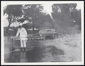 Traffic barrier is erected by workman outside Boston's Civil Defense Headquarters at White Stadium as storm-brought flood inundates Playstead Rd., an approach to the stadium.