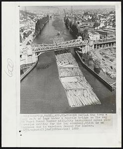 Seattle, Wash. -- Timber Haul -- A tug tows a huge raft of logs under a Seattle bridge on its way to Puget Sound lumber mill. City background makes picturesque setting for the log movement, which is on increase due to war-born demand for lumber.