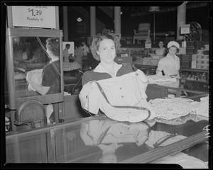 Unidentified woman holding dress behind department store counter