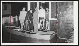 Melrose Evacuation-Auxiliary Fireman Louis Restuecia steadies boat for Richardson family pf 45 Groveland Rd., Melrose. Their home was flooded last night by overflow of Spot Pond. Left to right, James Richardson, Restuecia, Charles Richardson, Mrs. Richardson and William Richardson.