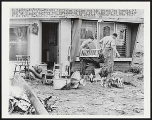 Tom Collins and his friend Don Bennett, (L) wearing hip boots, carry out furnishings, owned by Collins out of his trailer home at Klamath Glen near here 12/27. With weather turning cold, they built a log fire (L-fgnd.) to keep warm.